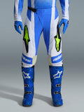 Alpinestars 2026 Techstar Knif Pants, spodnie motocrossowe, niebieskie UCLA, czarne i neonowe żółte, noszone z pasującymi niebieskimi rękawicami i butami, białe panele i wyraziste żółte logo fluo, ergonomiczny krój wyścigowy do jazdy w terenie
