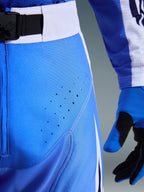 Spodnie Alpinestars 2026 Techstar Knif, kolor Ucla Blue i biały, zbliżenie na okolice bioder pokazujące laserowo wycięte perforacje wentylacyjne, magnetyczne zapięcie SX2 w pasie oraz pasujące rękawice motocrossowe
