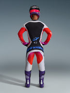 Alpinestars 2026 Techstar Knif Gear Set, kompletny strój motocrossowy widoczny od tyłu, biało-czarna koszulka z czerwonym gradientem na rękawach, białe spodnie z czerwonymi i różowymi akcentami, fioletowe buty i różowy kask, wyraźny niebieski branding, profesjonalny zestaw wyścigowy off-road