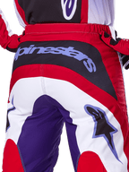 Alpinestars 2025 Fluid Wurx Pants, spodnie motocrossowe, fioletowe i jasnoczerwone, zbliżenie na tył z wyraźnym logo Alpinestars na czarnym panelu siedzenia, wzór z blokami kolorów w odcieniach czerwieni, bieli i fioletu, profesjonalna odzież wyścigowa off-road