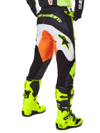 Alpinestars 2025 Fluid Wurx Pants, spodnie motocrossowe, żółto-czarne z pomarańczowymi i białymi akcentami, widok z tyłu, prezentowane z pasującymi jaskrawożółtymi butami, wytrzymała konstrukcja z wyraźnym brandingiem do jazdy na motocyklu terenowym