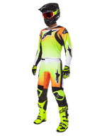 Zawodnik motocrossowy w spodniach Alpinestars 2025 Fluid Wurx w kolorze żółto-czarnym, wyrazisty gradient od żółtego do białego z pomarańczowymi i czarnymi akcentami, kompletny zestaw wyścigowy z pasującą koszulką, czarnym kaskiem i neonowo-żółtymi butami