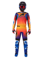 Alpinestars 2025 Fluid Wurx Pants, spodnie motocrossowe, wielokolorowy gradient pomarańczowo-żółto-fioletowy, noszone z pasującą bluzą, czarny kask z niebieskimi goglami, czerwono-czarne rękawice i niebieskie buty, kompletny zestaw odzieży motocrossowej