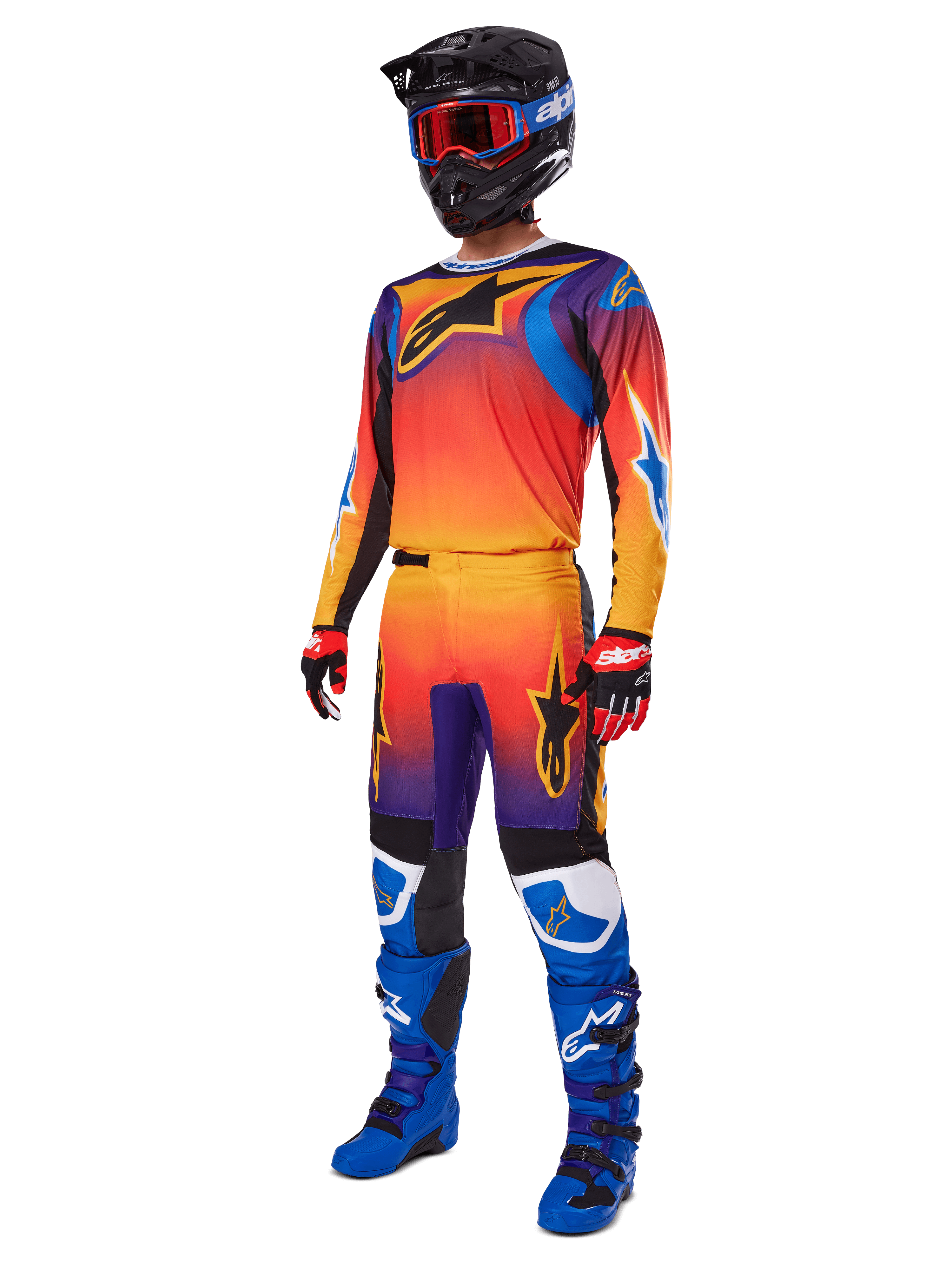 Zawodnik motocrossowy ubrany w kompletny strój wyścigowy, spodnie Alpinestars Fluid Wurx 2025 i dopasowana koszulka w wielokolorowym gradiencie pomarańczowym, czerwonym i fioletowym, czarny kask z czerwonymi goglami, niebiesko-czarne buty, czerwono-czarne rękawice, skoordynowany zestaw do wyścigów terenowych