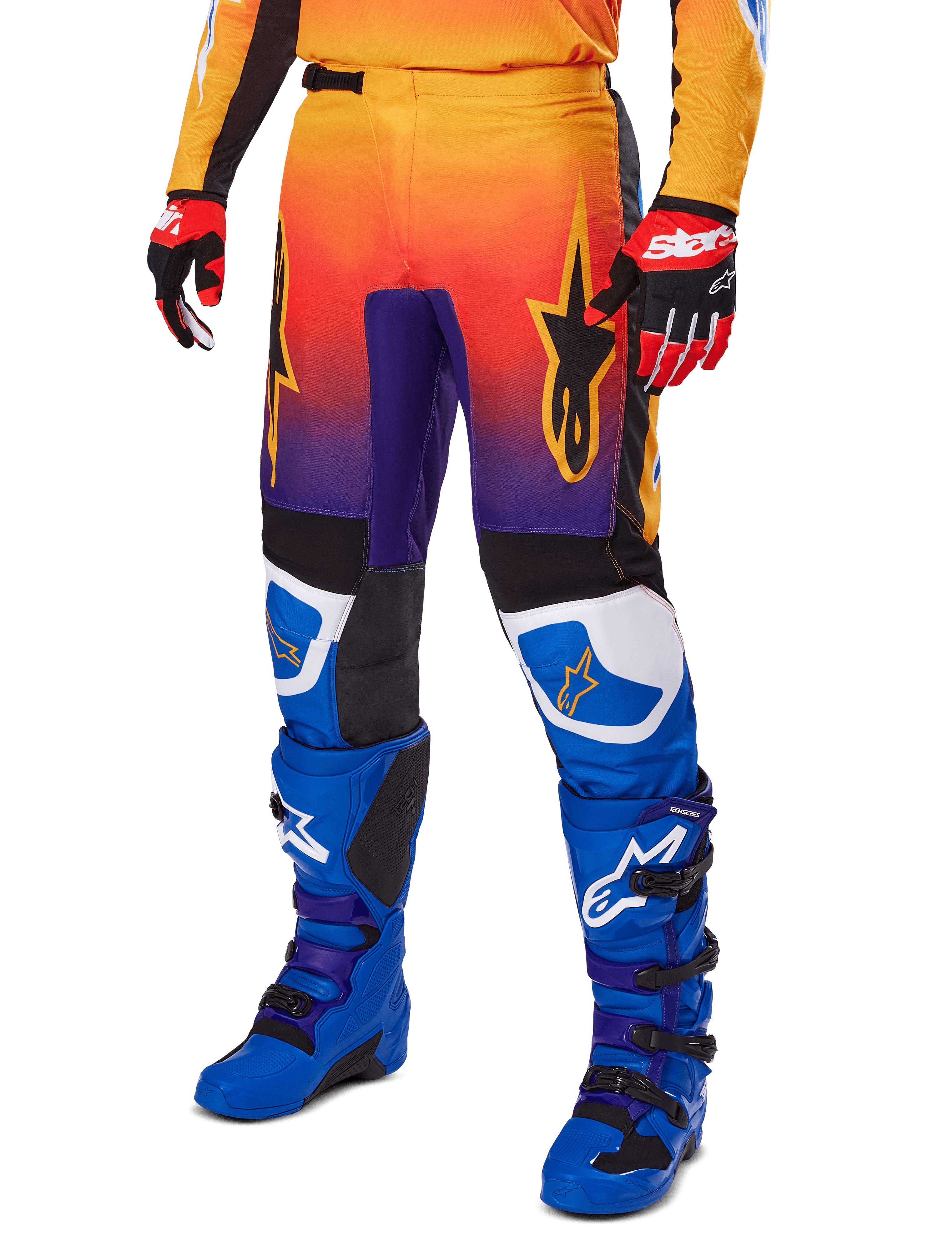 Alpinestars 2025 Fluid Wurx Pants, spodnie motocrossowe, wielokolorowy gradient pomarańczowo-czerwony i fioletowy z czarnymi i niebieskimi panelami, noszone z niebieskimi butami i czerwonymi rękawicami, grafiki z logo gwiazdy i białe akcenty na kolanach, wytrzymała odzież wyczynowa do wyścigów terenowych