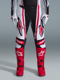 Alpinestars 2026 Techstar Nomur Pants, spodnie motocrossowe, czarno-biało-czerwone, noszone z dopasowanymi czerwonymi butami i białymi rękawicami, z wyraźnymi czerwonymi logo na udach i brandingiem „astars” na kolanach, wielopanelowa konstrukcja wyścigowa do jazdy w terenie