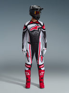 Zestaw Alpinestars 2026 Techstar Nomur, zawodnik motocrossowy w pełnym stroju wyścigowym, czarno-biało-czerwony design z białym nakrapianym wzorem, koszulka z czerwonym logo Astars, pasujące biało-czerwone spodnie, jaskrawoczerwone buty i czarny kask z goglami, profesjonalny zestaw motocrossowy