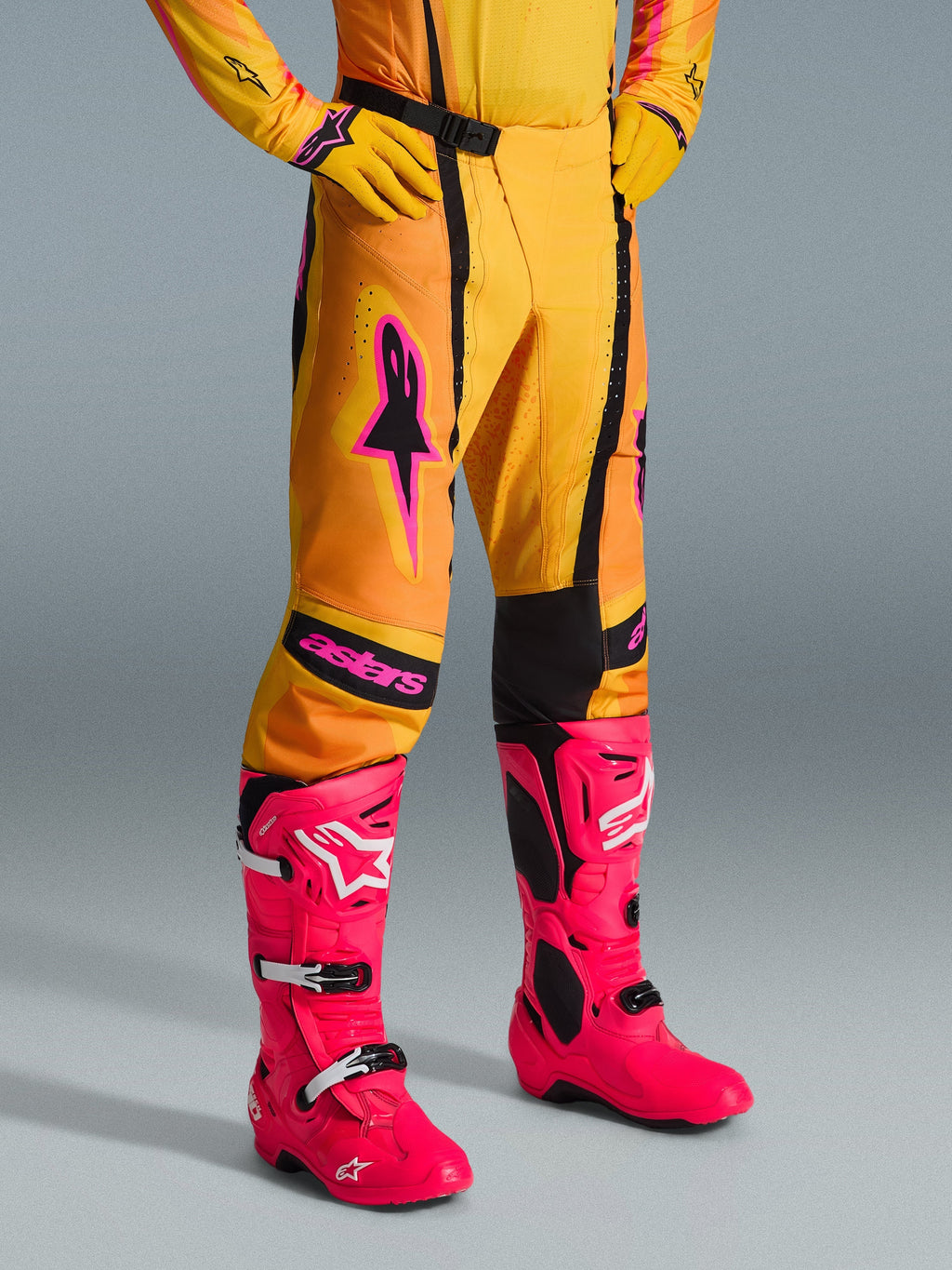 Alpinestars 2026 Techstar Nomur Pants, spodnie motocrossowe, pomarańczowo-żółto-różowe, zestawione z pasującą żółtą koszulką i rękawicami oraz jaskraworóżowymi butami, atletyczny krój wyścigowy z różowym logo i czarną magnetyczną klamrą, wyrazista odzież do rywalizacji w terenie