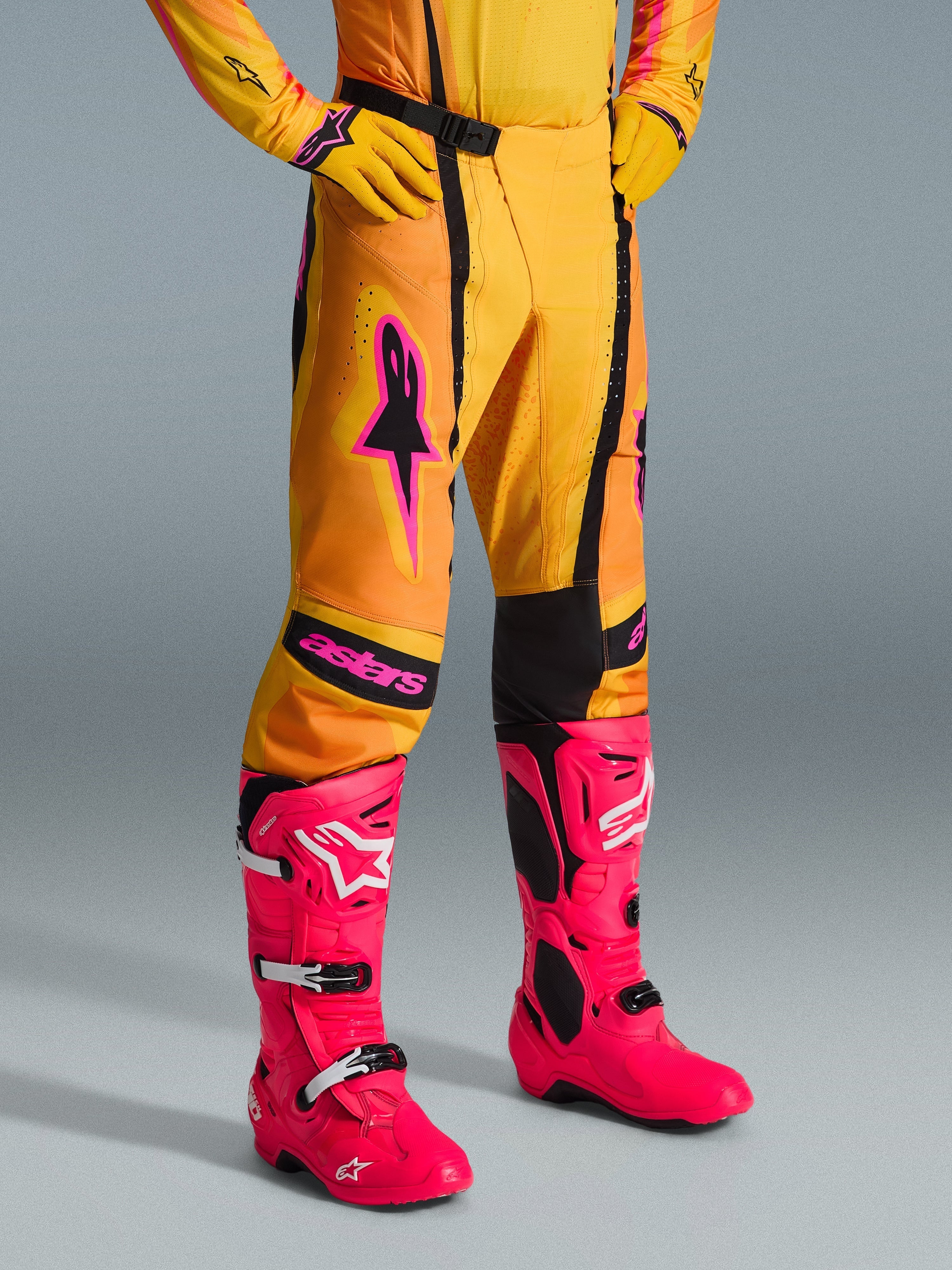 Alpinestars 2026 Techstar Nomur Pants, spodnie motocrossowe, pomarańczowo-żółto-różowe, zestawione z pasującą żółtą koszulką i rękawicami oraz jaskraworóżowymi butami, atletyczny krój wyścigowy z różowym logo i czarną magnetyczną klamrą, wyrazista odzież do rywalizacji w terenie