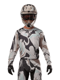 Alpinestars Racer Tactical Jersey 2024, koszulka motocrossowa, wzór moro Iron Camo Dust Gray, zawodnik w dopasowanym kasku i goglach oraz czarnych rękawicach, techniczna odzież do wyścigów terenowych