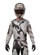 Alpinestars Racer Tactical Jersey 2024, koszulka motocrossowa, wzór moro Iron Camo Dust Gray, zawodnik w dopasowanym kasku i goglach oraz czarnych rękawicach, techniczna odzież do wyścigów terenowych