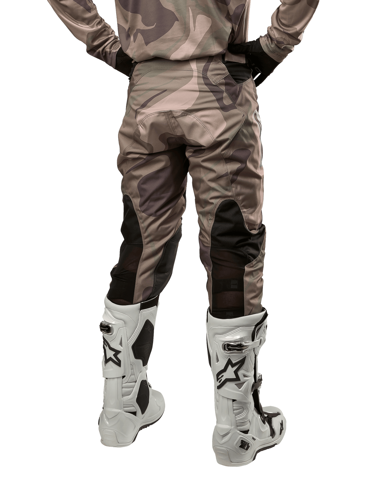 Spodnie Alpinestars Racer Tactical 2024, spodnie motocrossowe, Military Green Camo Brown, widok z tyłu prezentujący wzór kamuflażu oraz czarne, oddychające panele elastyczne na dolnej części nogawek, noszone z białymi butami motocrossowymi, wytrzymała odzież techniczna do jazdy terenowej