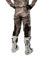 Spodnie Alpinestars Racer Tactical 2024, spodnie motocrossowe, Military Green Camo Brown, widok z tyłu prezentujący wzór kamuflażu oraz czarne, oddychające panele elastyczne na dolnej części nogawek, noszone z białymi butami motocrossowymi, wytrzymała odzież techniczna do jazdy terenowej
