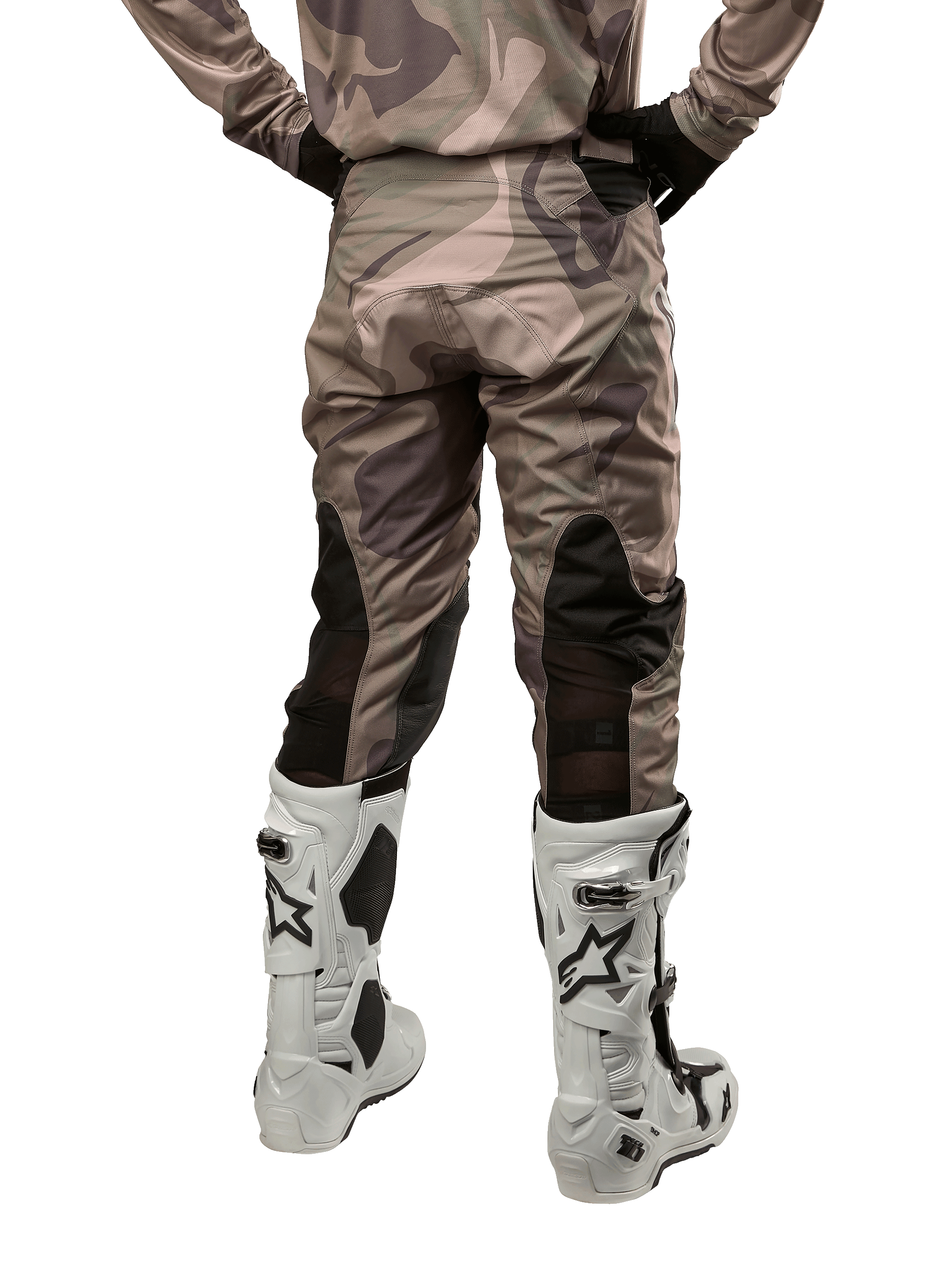 Spodnie Alpinestars Racer Tactical 2024, spodnie motocrossowe, Military Green Camo Brown, widok z tyłu prezentujący wzór kamuflażu oraz czarne, oddychające panele elastyczne na dolnej części nogawek, noszone z białymi butami motocrossowymi, wytrzymała odzież techniczna do jazdy terenowej