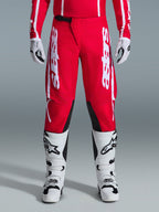 Alpinestars 2026 Fluid Apex Pants, spodnie motocrossowe, czerwono-białe, z dużymi białymi logo Astars na udach i czarnymi panelami po wewnętrznej stronie kolan, noszone z pasującymi biało-czarnymi butami i rękawicami dla pełnego zestawu wyścigowego off-road