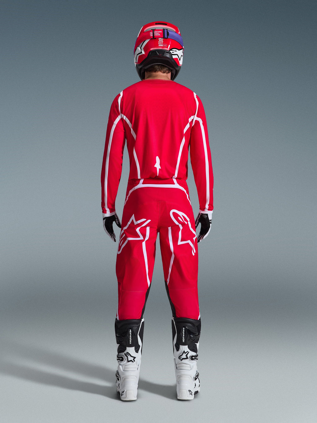 Alpinestars 2026 Fluid Apex Pants, spodnie motocrossowe, czerwono-białe, widok z tyłu z pasującą koszulką, czerwonym kaskiem i biało-czarnymi butami, duże białe logo Astar na nogawkach, skoordynowany strój do wyścigów off-road