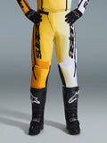 Alpinestars 2026 Fluid Apex Pants, spodnie motocrossowe, żółto-czarne, dwukolorowy design z żółtymi i białymi panelami, wyraźne pionowe logo „astars”, noszone z czarnymi butami i rękawicami motocrossowymi, odzież wyczynowa do jazdy terenowej