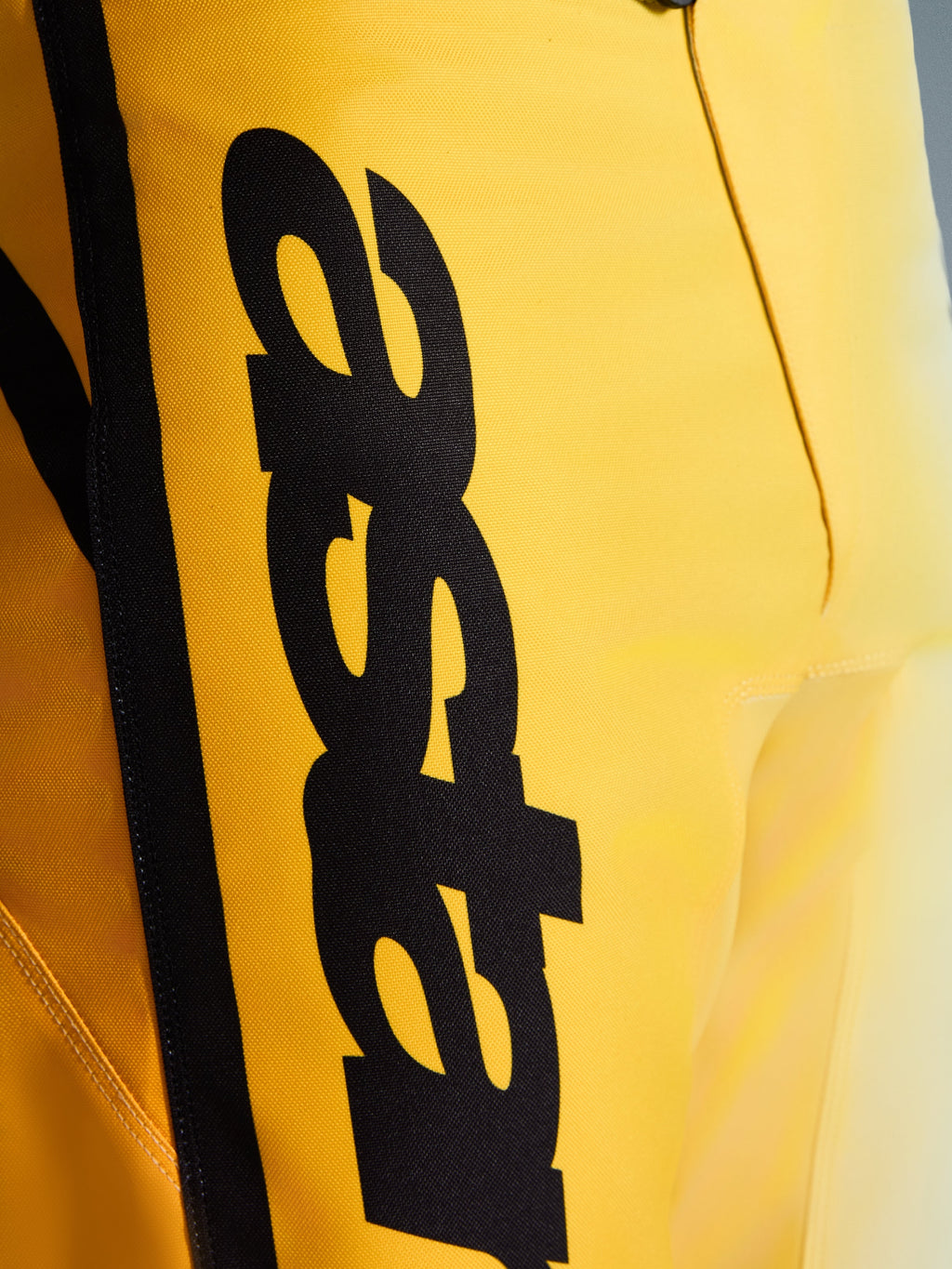 Zbliżenie na spodnie Alpinestars 2026 Fluid Apex, spodnie motocrossowe, żółto-czarne, z dużym pionowym czarnym logo, wytrzymałym teksturowanym materiałem i ergonomicznymi detalami zapewniającymi wydajność w terenie