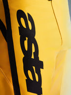 Zbliżenie na spodnie Alpinestars 2026 Fluid Apex, spodnie motocrossowe, żółto-czarne, z dużym pionowym czarnym logo, wytrzymałym teksturowanym materiałem i ergonomicznymi detalami zapewniającymi wydajność w terenie