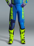 Alpinestars 2026 Fluid Apex Pants, spodnie motocrossowe, niebieskie i żółte fluo, noszone z pasującymi żółtymi butami fluo i fioletowymi rękawicami, wyraźne żółte logo na bokach, ergonomiczna konstrukcja do wyścigów terenowych