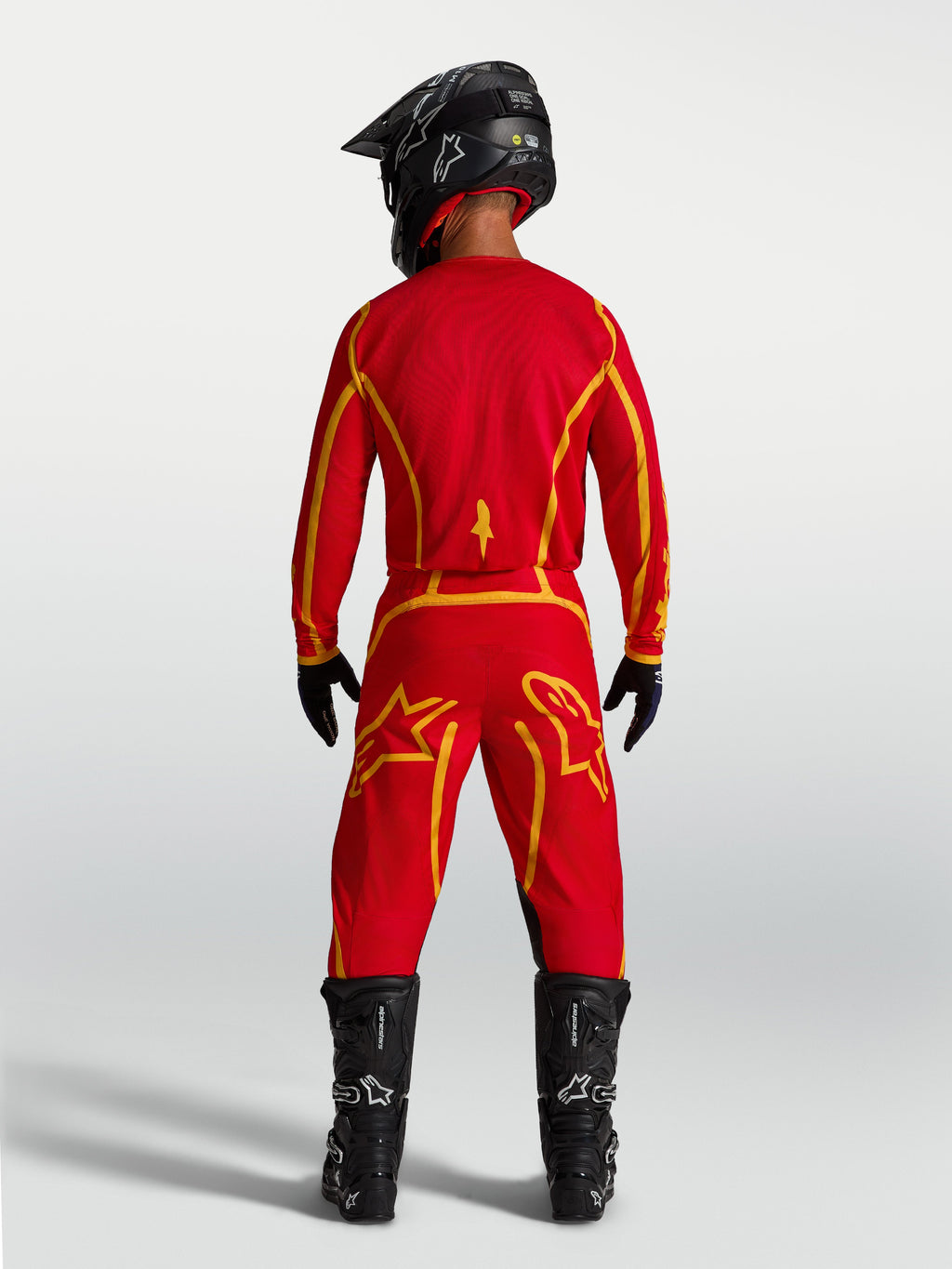 Alpinestars Spodnie Fluid Apex V2, męskie spodnie motocrossowe, czerwone i złote, ergonomiczny sportowy krój ze wzmocnionym siedzeniem, widok od tyłu na modelu w pełnym sprzęcie MX.