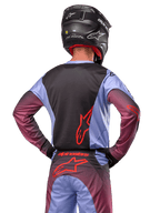 Zawodnik motocrossowy od tyłu w stroju Alpinestars 2024 Racer Hoen, fioletowo-czarna koszulka z czerwonym logo, pasujące spodnie z czerwonymi akcentami, czarny kask, dopasowany strój do wyścigów terenowych