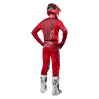 Spodnie Alpinestars Racer Hoen 2024 i dopasowana koszulka w kolorze Mars Red Burgundy, widok z tyłu zawodnika motocrossowego w pełnym stroju, w tym w czerwonym kasku i białych butach, prezentujący sportowy krój i branding do wyścigów terenowych.