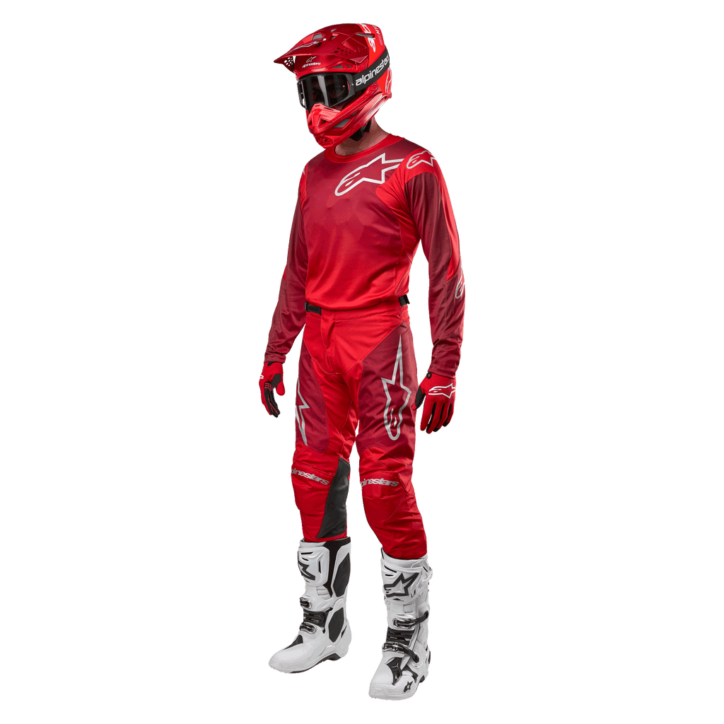 Motocyklista motocrossowy w pełnym stroju wyścigowym, spodnie i bluza Alpinestars Racer Hoen 2024 w kolorze Mars Red Burgundy, czerwony kask, czerwone rękawice oraz biało-czarne buty, dopasowany zestaw do wyścigów terenowych