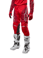 Alpinestars 2024 Racer Hoen Pants, spodnie motocrossowe, w kolorze Mars Red i bordowym, zestawione z pasującą czerwoną koszulką, rękawicami i białymi butami, wyposażone w czarne skórzane panele na kolanach i białe logo, wytrzymały sprzęt techniczny do wyścigów terenowych
