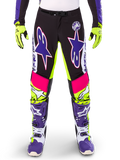 Alpinestars Limited Edition Supertech Dirt Studios Pants, spodnie motocrossowe, białe, fioletowe i żółte fluo, czarne panele z neonowo-żółtymi i różowymi akcentami, duże fioletowe logo gwiazdy, widoczne z pasującymi neonowo-żółtymi rękawicami i fioletowymi butami wyścigowymi, wytrzymała odzież wyścigowa off-road