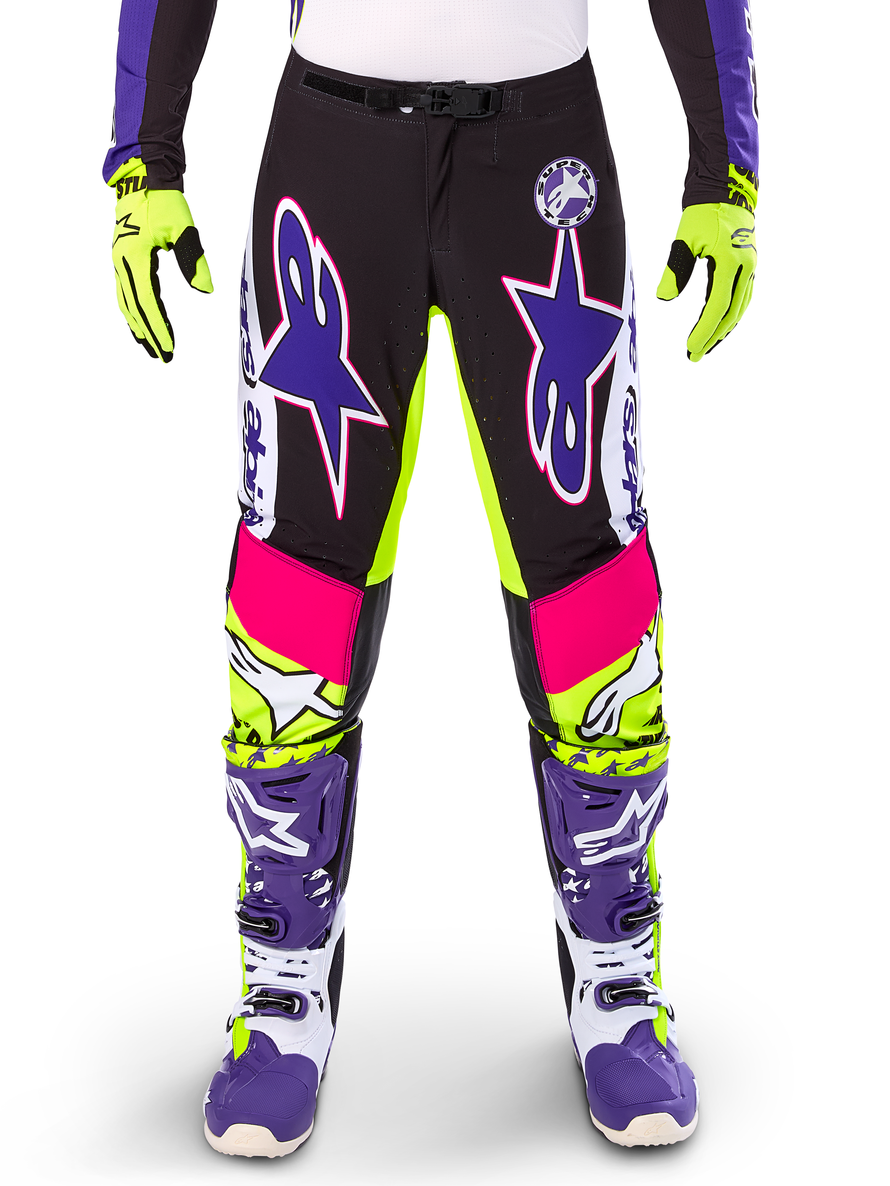 Alpinestars Limited Edition Supertech Dirt Studios Pants, spodnie motocrossowe, białe, fioletowe i żółte fluo, czarne panele z neonowo-żółtymi i różowymi akcentami, duże fioletowe logo gwiazdy, widoczne z pasującymi neonowo-żółtymi rękawicami i fioletowymi butami wyścigowymi, wytrzymała odzież wyścigowa off-road