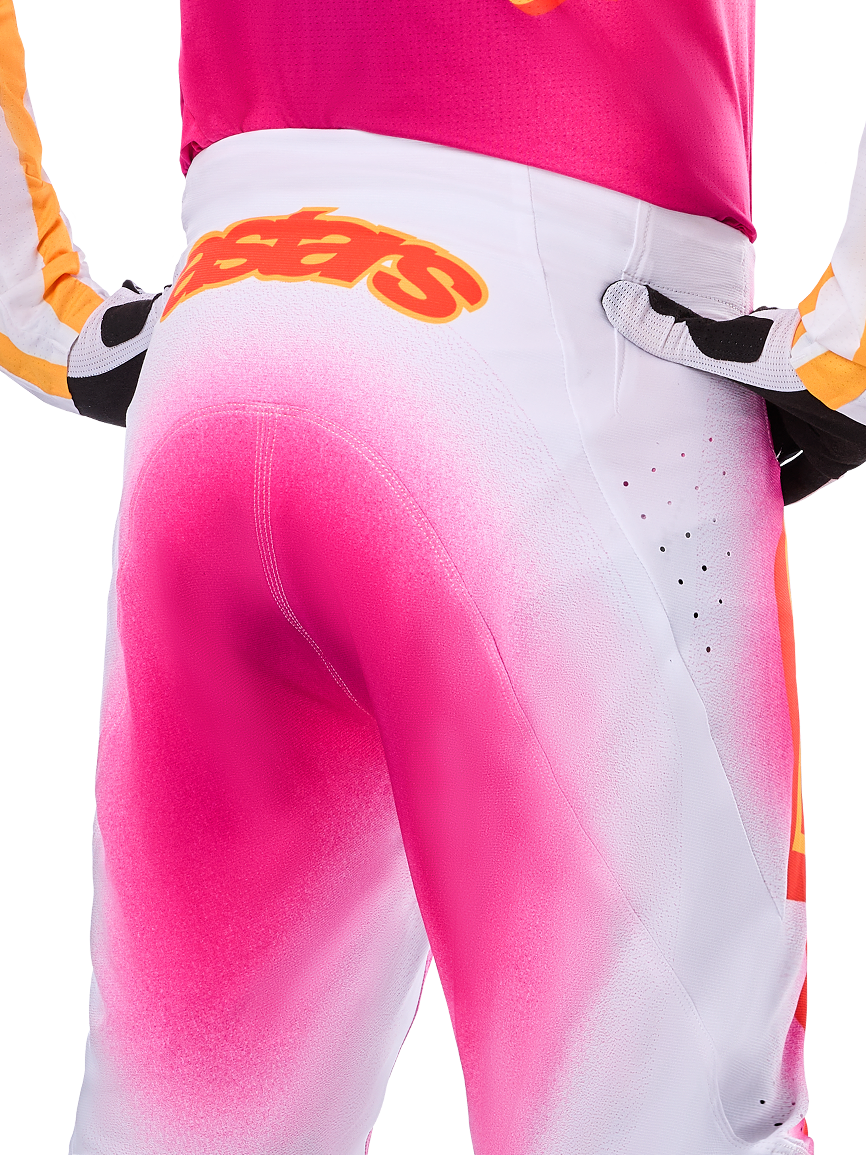 Alpinestars Limited Edition Supertech AFD MIG Pants, Motocross Pants, Pink Fluo and White with a spray-paint fade effect, large orange Alpinestars logo on the rear waistband, close-up view showing athletic fit and ventilation perforations.