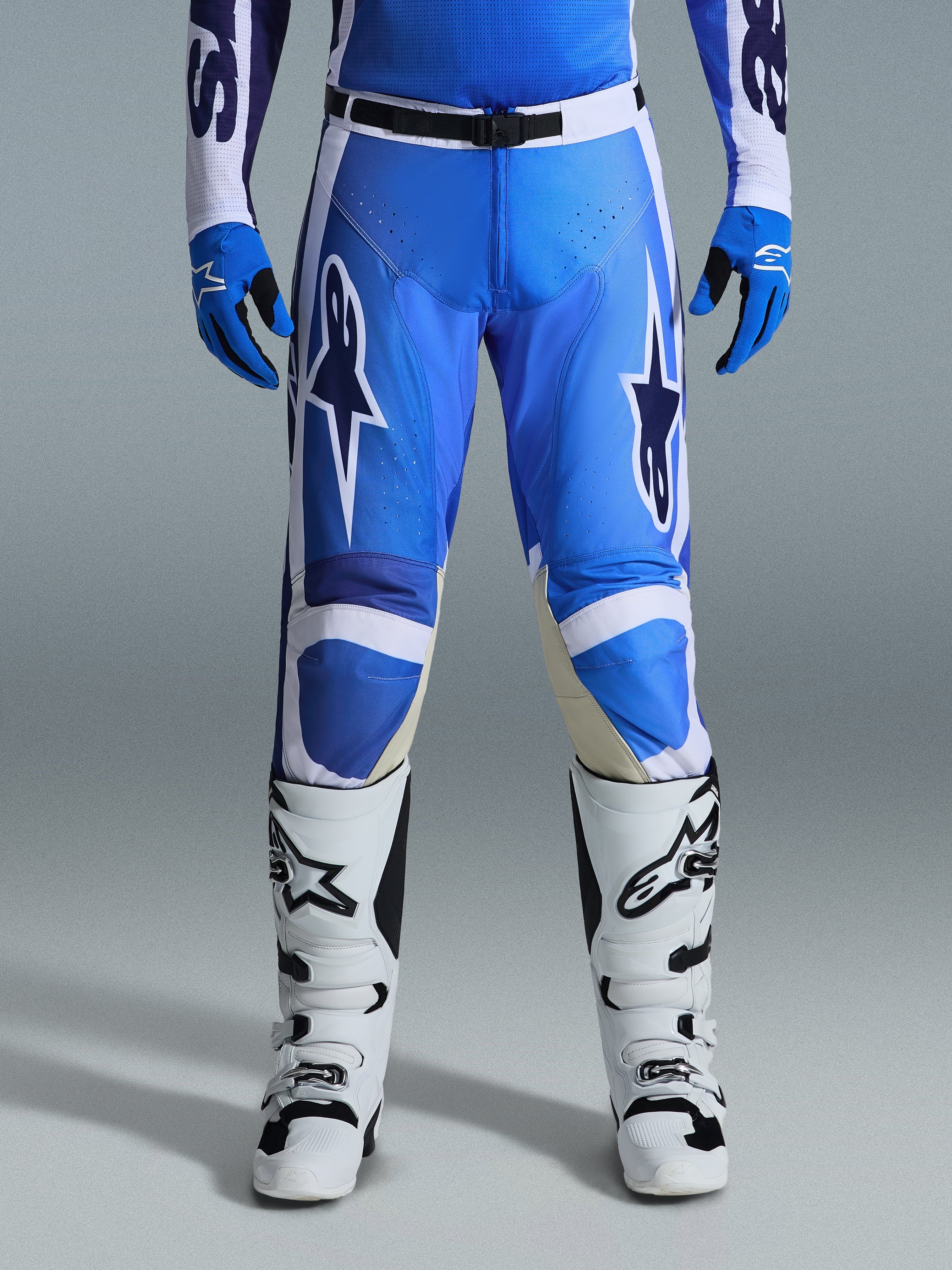 Alpinestars 2026 Racer Air Portl Pants, spodnie motocrossowe, niebiesko-białe, noszone z pasującymi niebieskimi rękawicami i białymi butami, czarne zapięcie w pasie, duże białe logo gwiazdy na udach, perforowany materiał zapewniający lepszy przepływ powietrza podczas wyścigów off-road