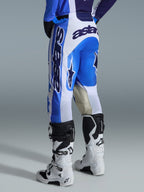 Alpinestars 2026 Racer Air Portl Pants, spodnie motocrossowe, kolorystyka Ucla Blue White, widok z tyłu, wyrazisty niebiesko-biały design z dużym logo na siedzeniu i boku, wzmocnienia z koziej skóry na wewnętrznej stronie kolan, noszone z biało-czarnymi butami motocrossowymi