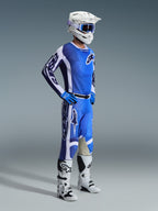 Zawodnik motocrossowy ubrany w spodnie 2026 Racer Air Portl w kolorystyce Ucla Blue White, zestawione z pasującą niebiesko-białą koszulką, białym kaskiem z niebieskimi goglami i białymi butami; pełny zestaw odzieży do wyścigów terenowych.