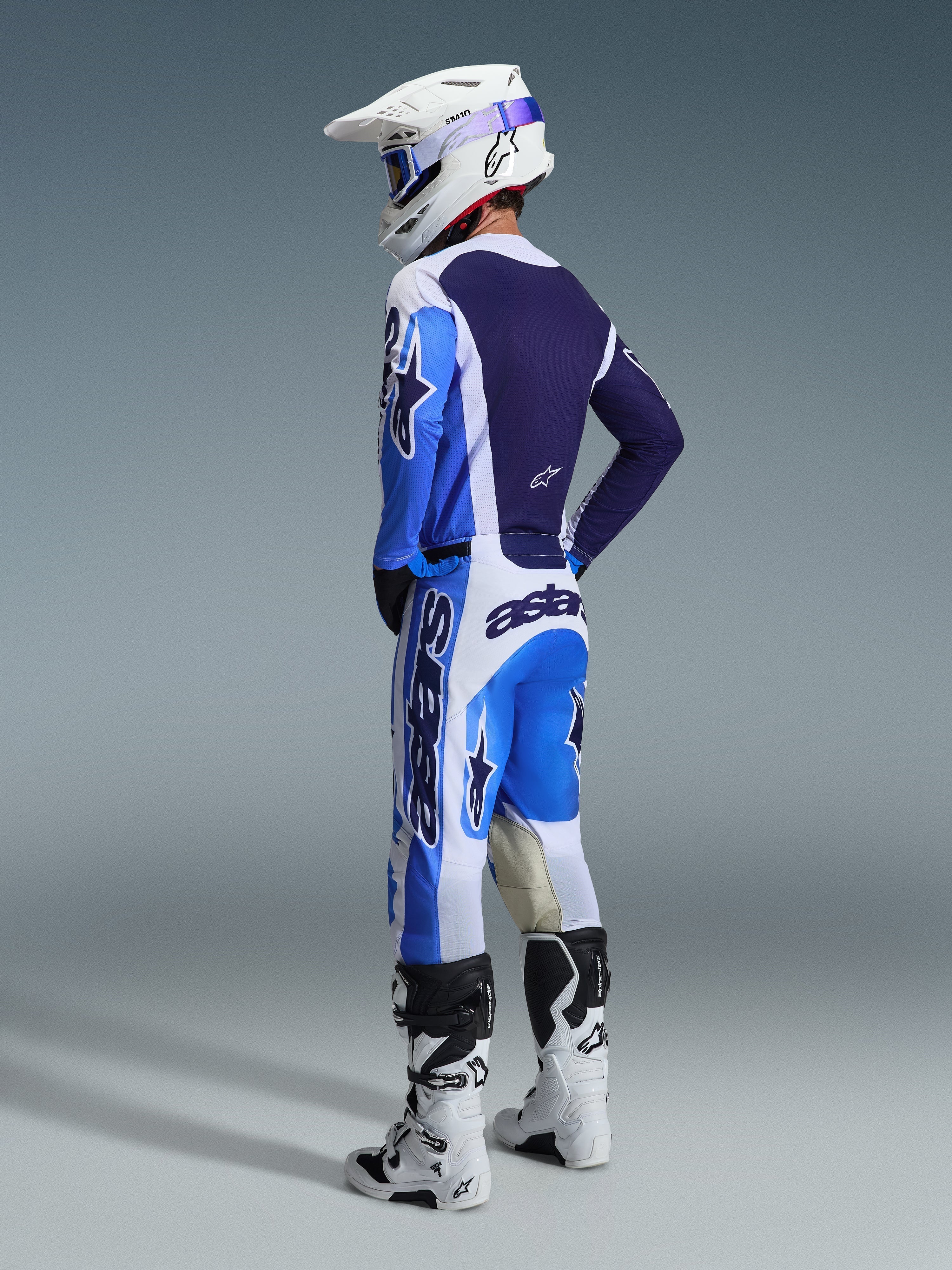 Spodnie Alpinestars 2026 Racer Air Portl, spodnie motocrossowe, niebiesko-białe, widok na zawodnika z tyłu i boku w pasującej bluzie, białym kasku i białych butach, wyraziste logo i siateczkowe panele wentylacyjne do wyścigów off-road