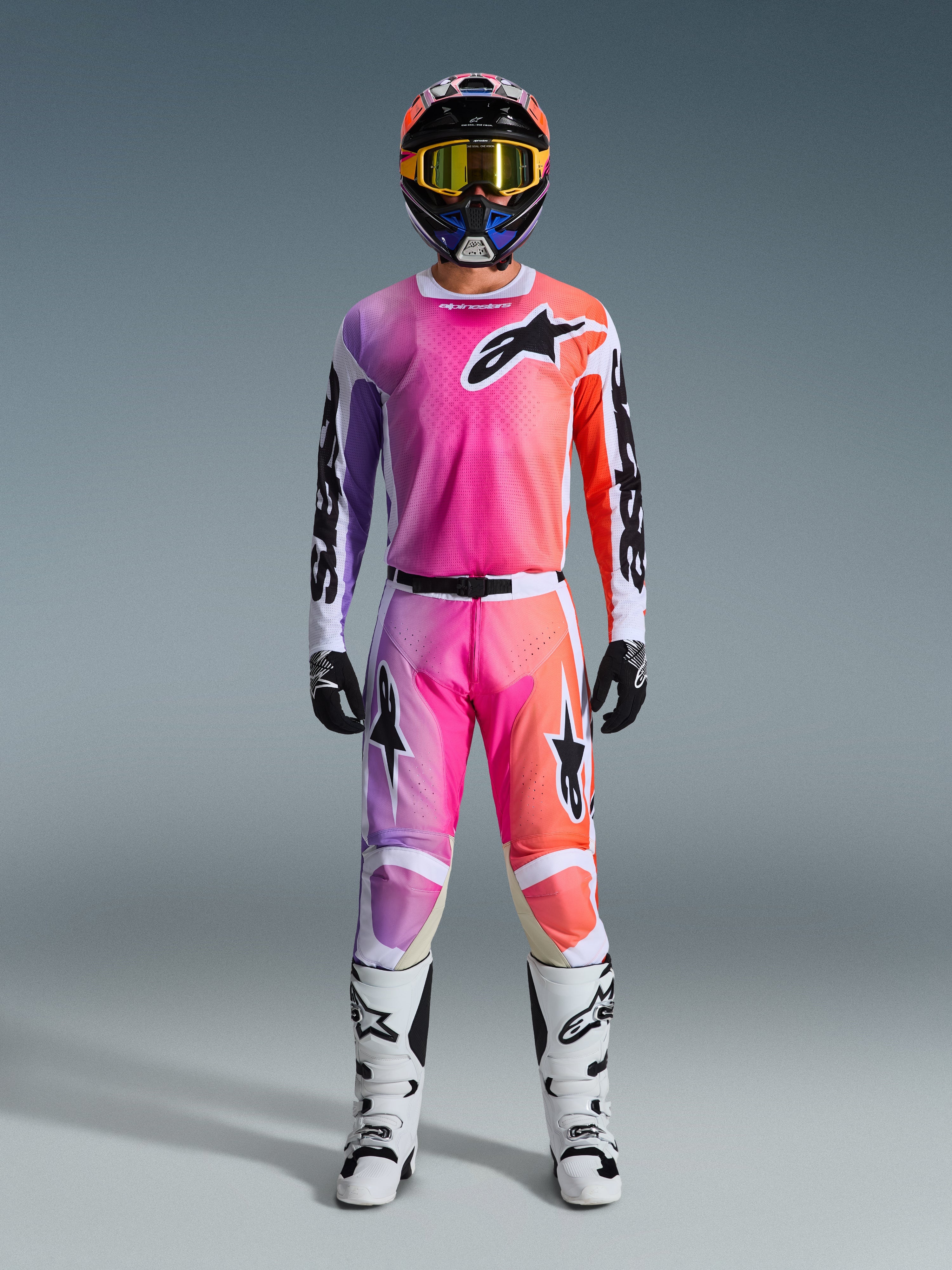 Zawodnik motocrossowy w koszulce 2026 Racer Air Portl i pasujących spodniach, różowy, fioletowy i pomarańczowy gradient z czarnym logo Alpinestars, białe buty wyścigowe, czarne rękawice i wielokolorowy kask, profesjonalny strój do wyścigów off-road