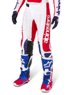 Alpinestars Limited Edition Techstar Fortitude Motocross Pants, spodnie motocrossowe, czerwono-biało-niebieska kolorystyka, noszone z dopasowanymi butami i rękawicami, pionowy branding Alpinestars, sportowy krój do wyścigów off-road