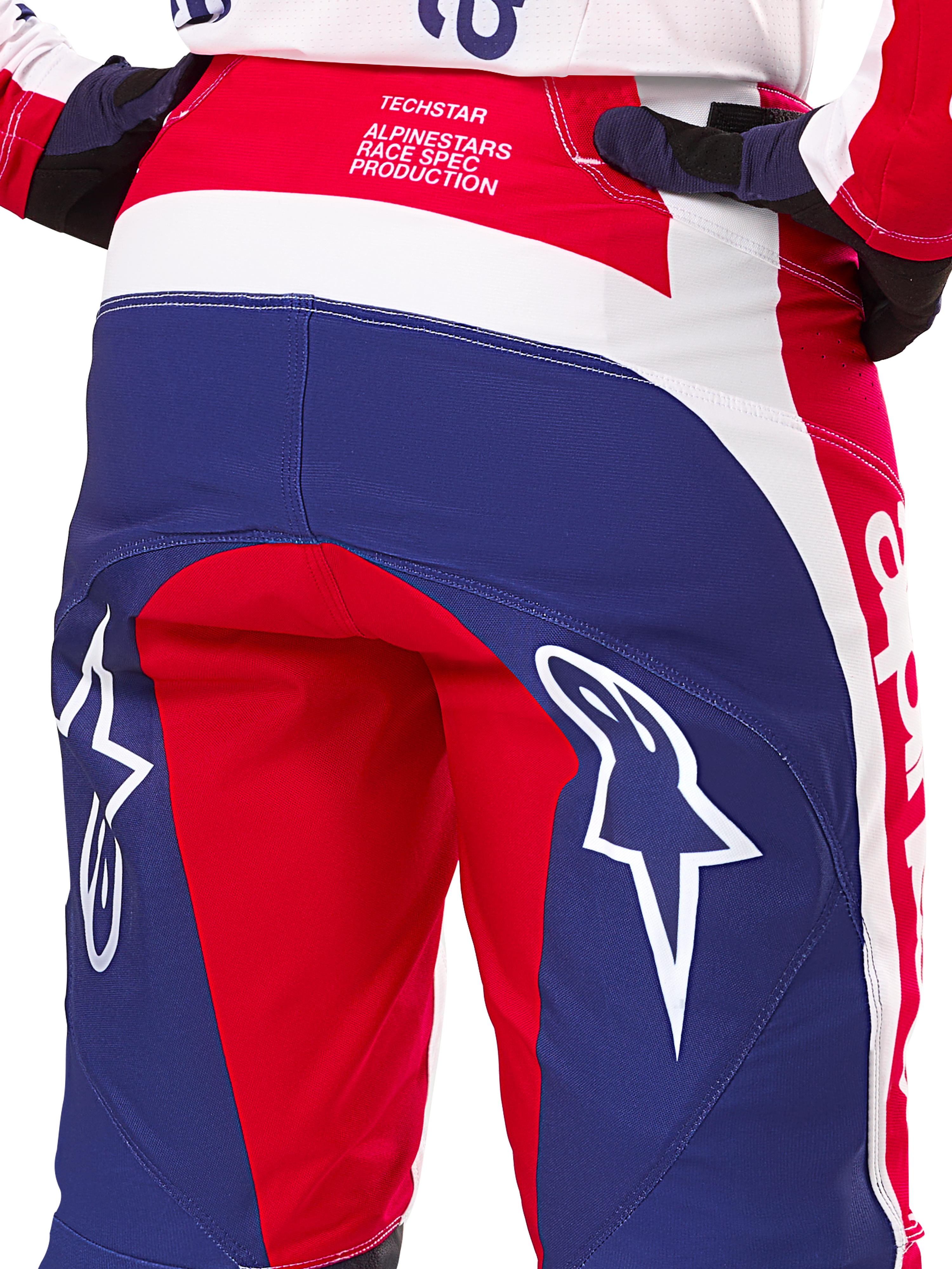 Spodnie Alpinestars Limited Edition Techstar Fortitude, spodnie motocrossowe, czerwone, białe i niebieskie, widok z tyłu z dużymi białymi logo gwiazdy na siedzisku oraz brandingiem Techstar Race Spec, wytrzymałe tekstylia techniczne do wyścigów off-road