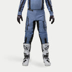 Alpinestars 2024 Fluid Lurv Pants, spodnie motocrossowe, jasnoniebieskie i czarne, noszone z biało-czarnymi butami wyścigowymi i dopasowanymi rękawicami, z wyraźnymi czarnymi logo gwiazdy na udach, ergonomiczna konstrukcja zapewniająca wydajność w terenie