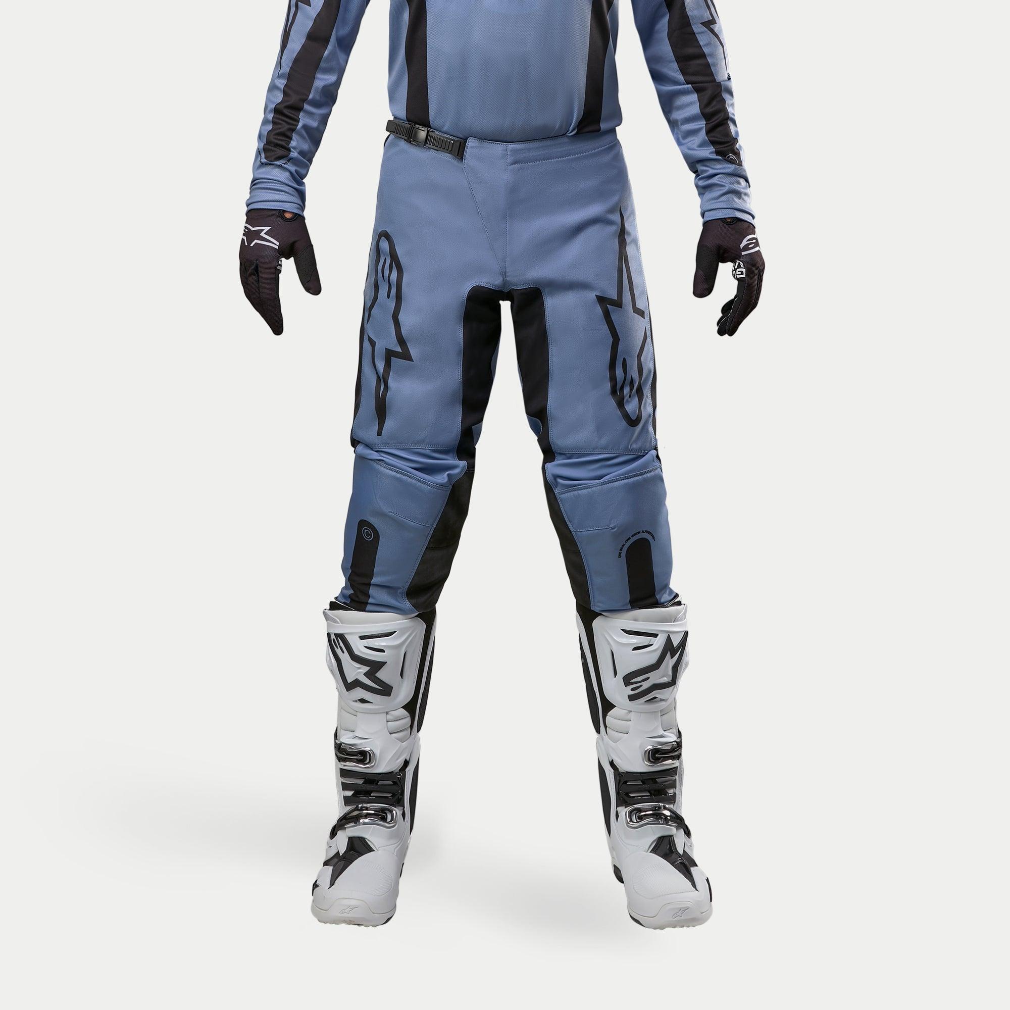 Alpinestars 2024 Fluid Lurv Pants, spodnie motocrossowe, jasnoniebieskie i czarne, noszone z biało-czarnymi butami wyścigowymi i dopasowanymi rękawicami, z wyraźnymi czarnymi logo gwiazdy na udach, ergonomiczna konstrukcja zapewniająca wydajność w terenie