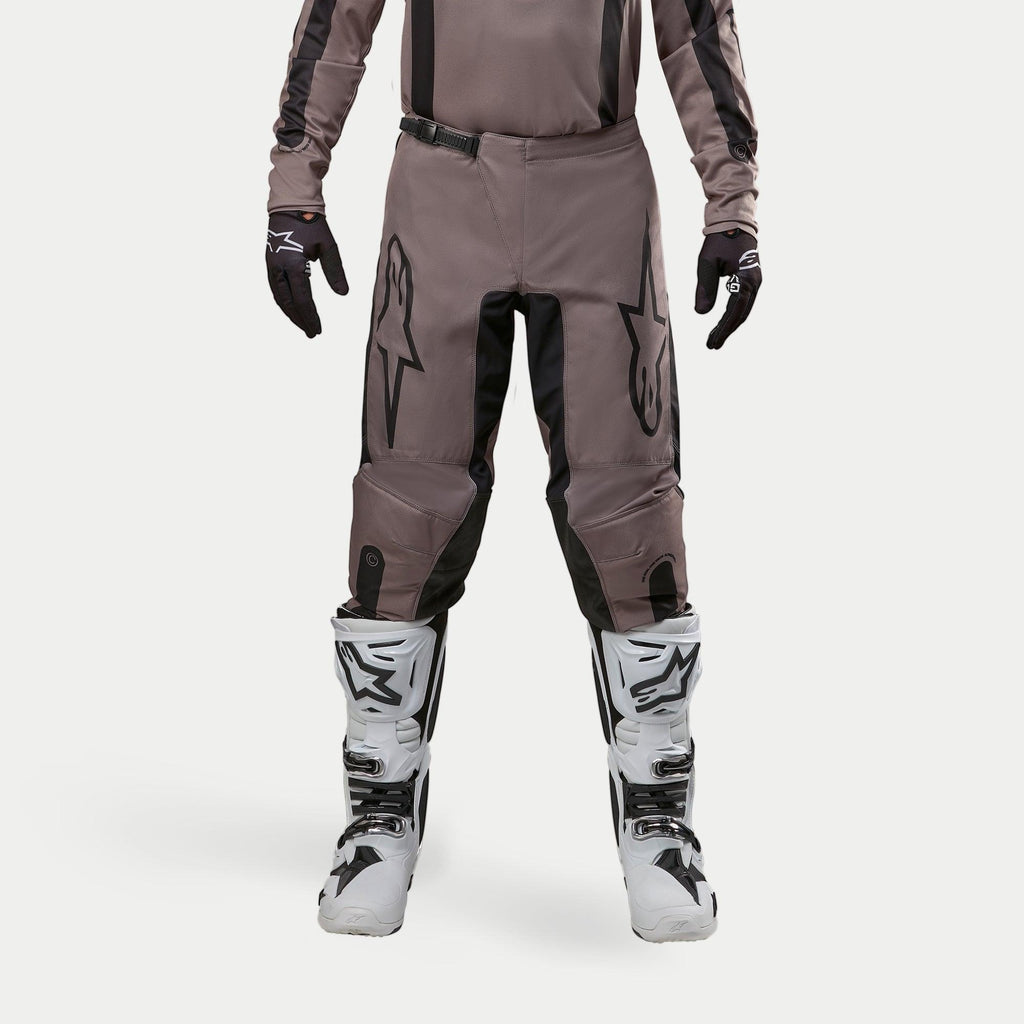 Alpinestars 2024 Fluid Lurv Pants, spodnie motocrossowe, Mud Black, noszone z pasującą bluzą, czarnymi rękawicami i białymi butami, duże czarne logo na udach, ergonomiczny krój i wytrzymały materiał do wyścigów off-road