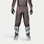 Alpinestars 2024 Fluid Lurv Pants, spodnie motocrossowe, Mud Black, noszone z pasującą bluzą, czarnymi rękawicami i białymi butami, duże czarne logo na udach, ergonomiczny krój i wytrzymały materiał do wyścigów off-road