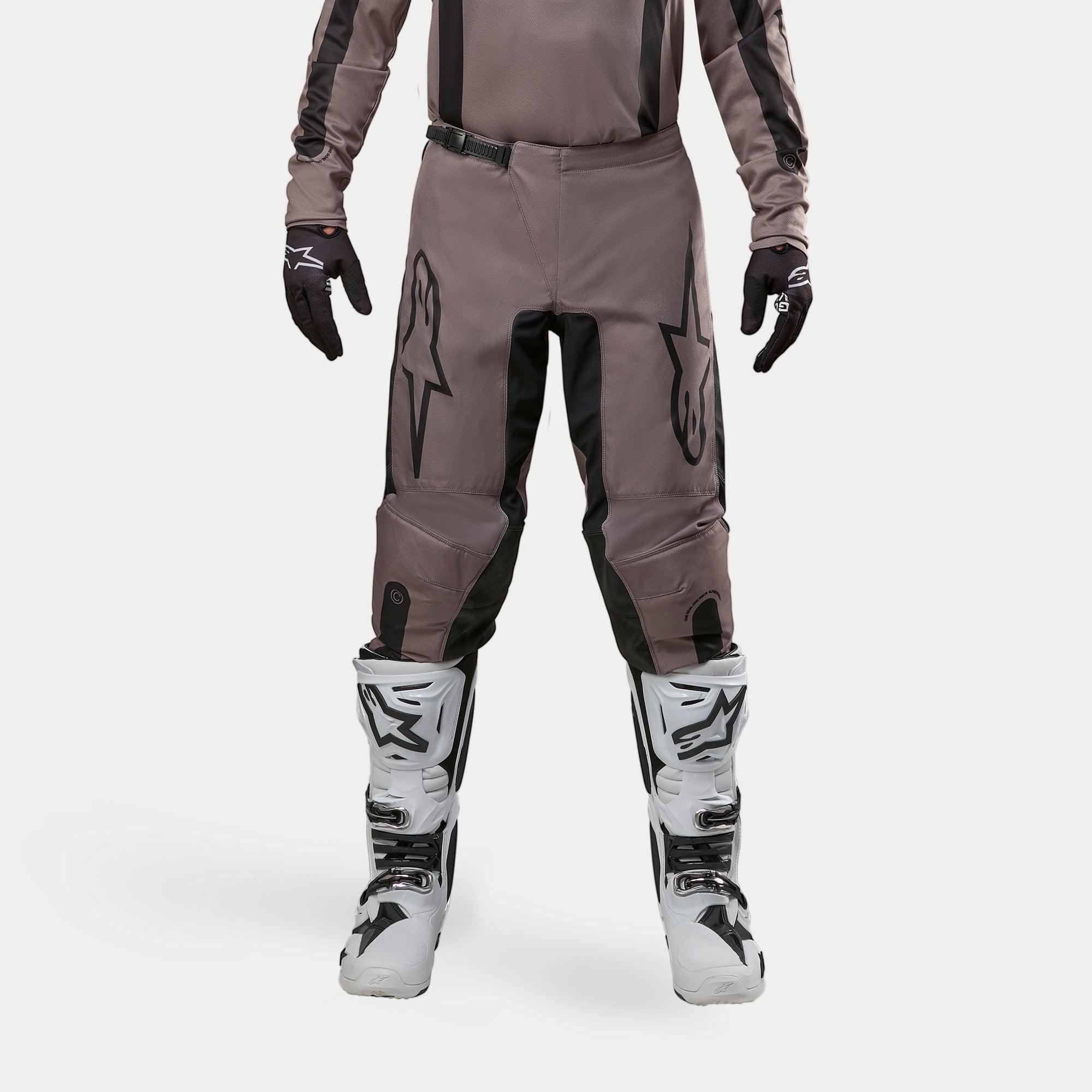 Alpinestars 2024 Fluid Lurv Pants, spodnie motocrossowe, Mud Black, noszone z pasującą bluzą, czarnymi rękawicami i białymi butami, duże czarne logo na udach, ergonomiczny krój i wytrzymały materiał do wyścigów off-road