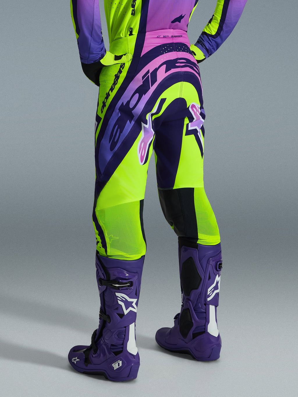 Alpinestars 2026 Supertech Vista Pants, spodnie motocrossowe, żółte, fioletowe i czarne, widok z tyłu, zestaw z pasującą koszulką i fioletowymi butami motocrossowymi, z wyraźnym brandingiem i oddychającymi strefami z siateczki na łydkach