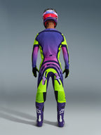 Alpinestars 2026 Supertech Vista Pants, spodnie motocrossowe, żółto-fioletowo-czarne, widok od tyłu zawodnika motocrossowego w pełnym zestawie wyścigowym z fioletową koszulką z gradientem i fioletowymi butami, wyrazisty sportowy design do profesjonalnych wyścigów off-road