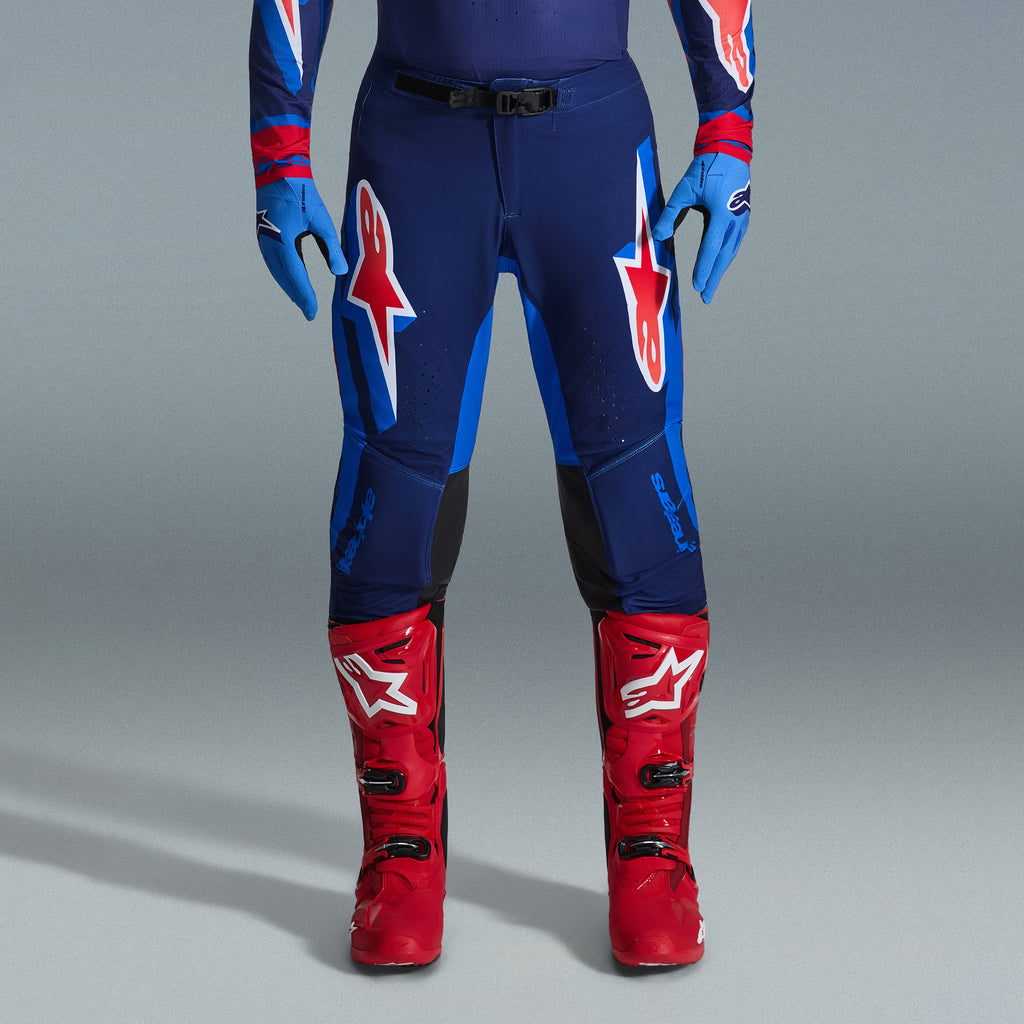 Zestaw Alpinestars 2026 Supertech Vista, spodnie motocrossowe w kolorze granatowym i jasnoniebieskim z czerwonymi i białymi logotypami, jasnoniebieskie rękawice i jaskrawoczerwone buty motocrossowe, profesjonalna odzież wyścigowa