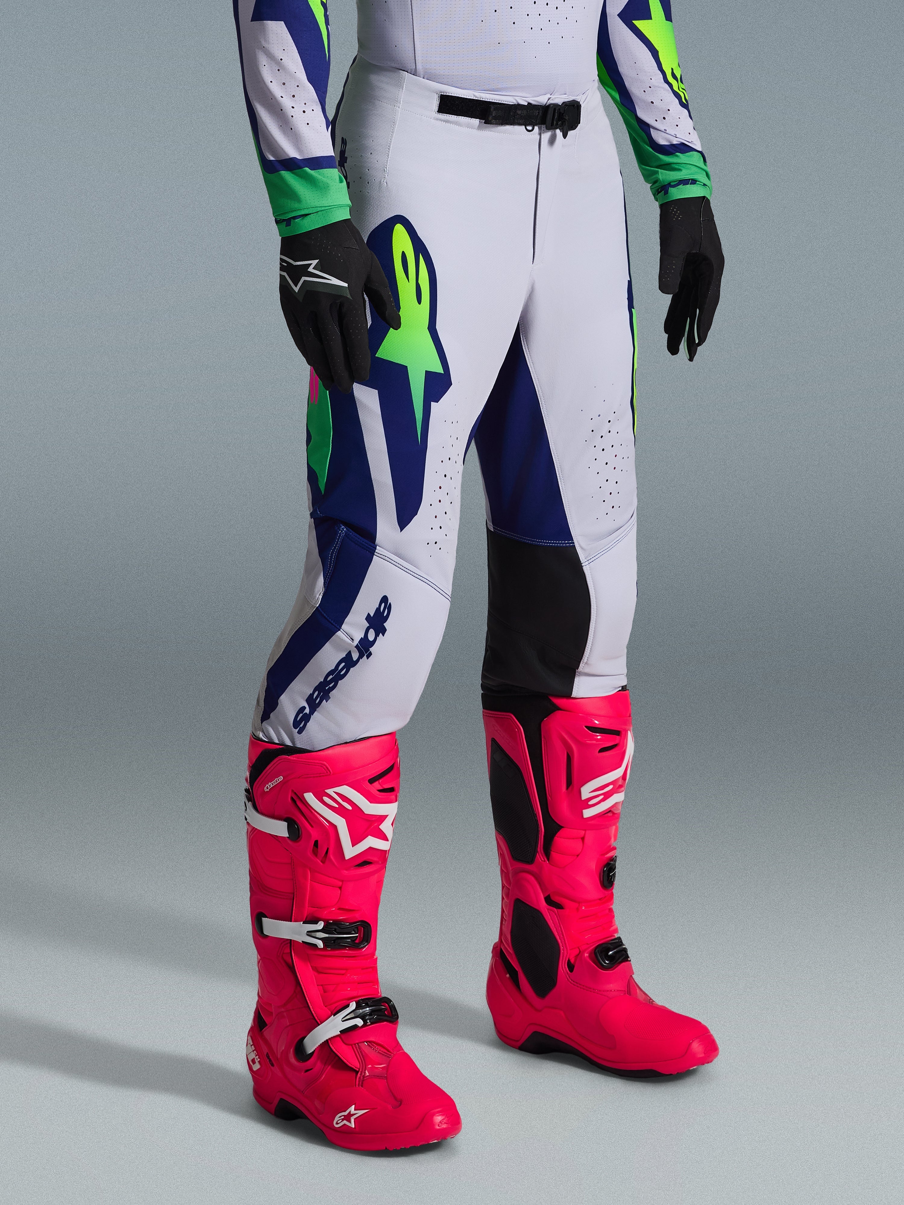 Zestaw Alpinestars 2026 Supertech Vista, spodnie motocrossowe, jasnoszare z granatowymi i limonkowymi akcentami, noszone z jaskraworóżowymi butami i czarnymi rękawicami, profesjonalny sportowy krój i wyraziste grafiki