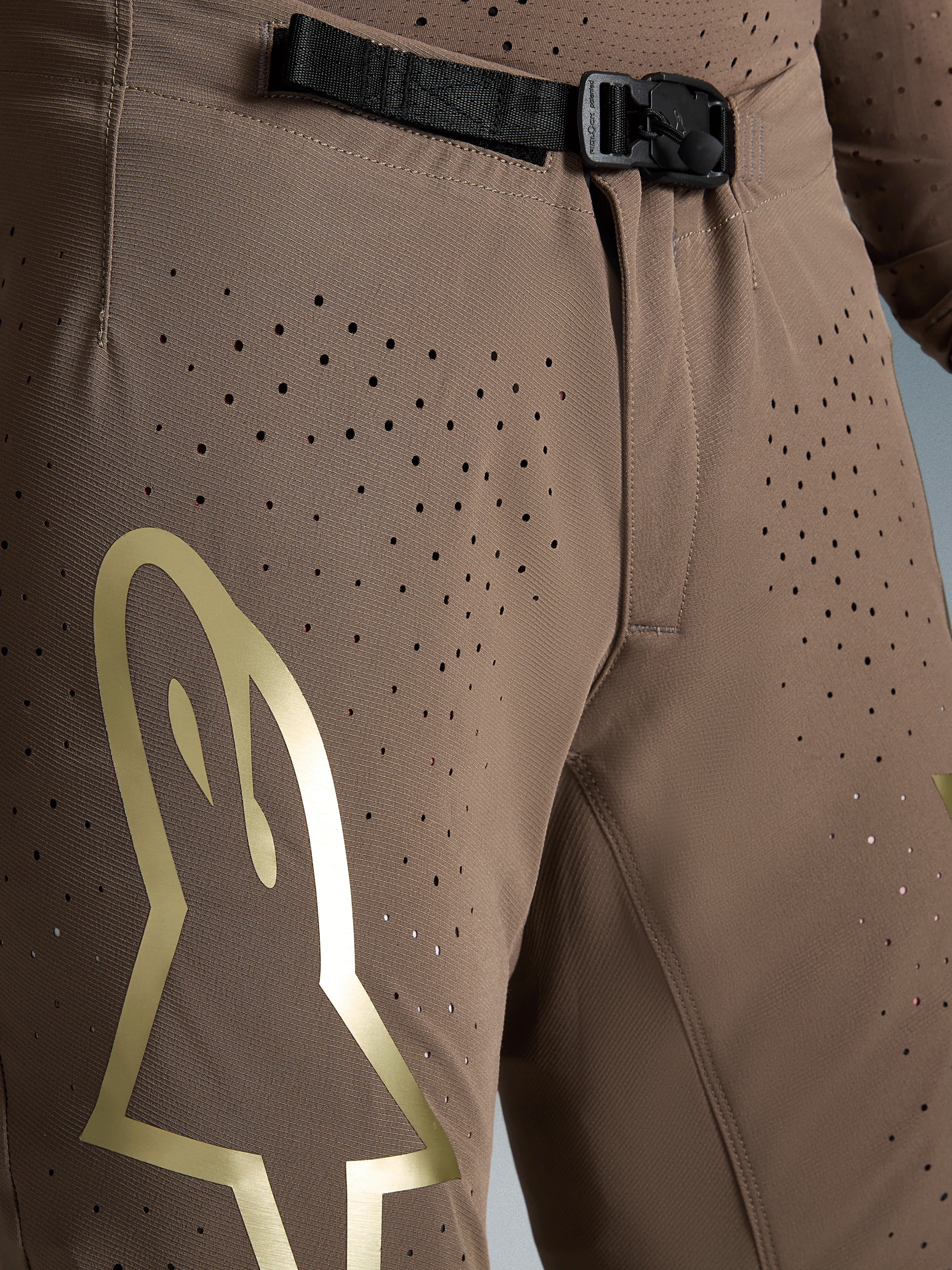 Alpinestars męskie spodnie Supertech Air Gold, brązowe ze złotym logo, klamra magnetyczna SX1 i perforacje.