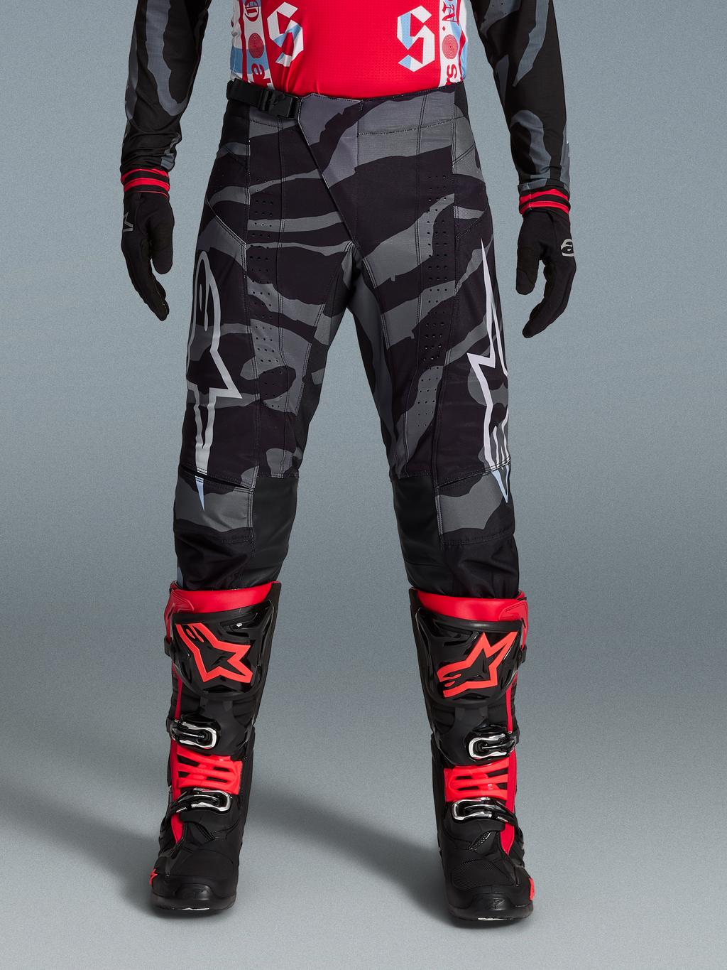 Spodnie Techstar Beast Coast Edycja Limitowana, szary wzór camo, czarno-czerwone buty MX i rękawice.